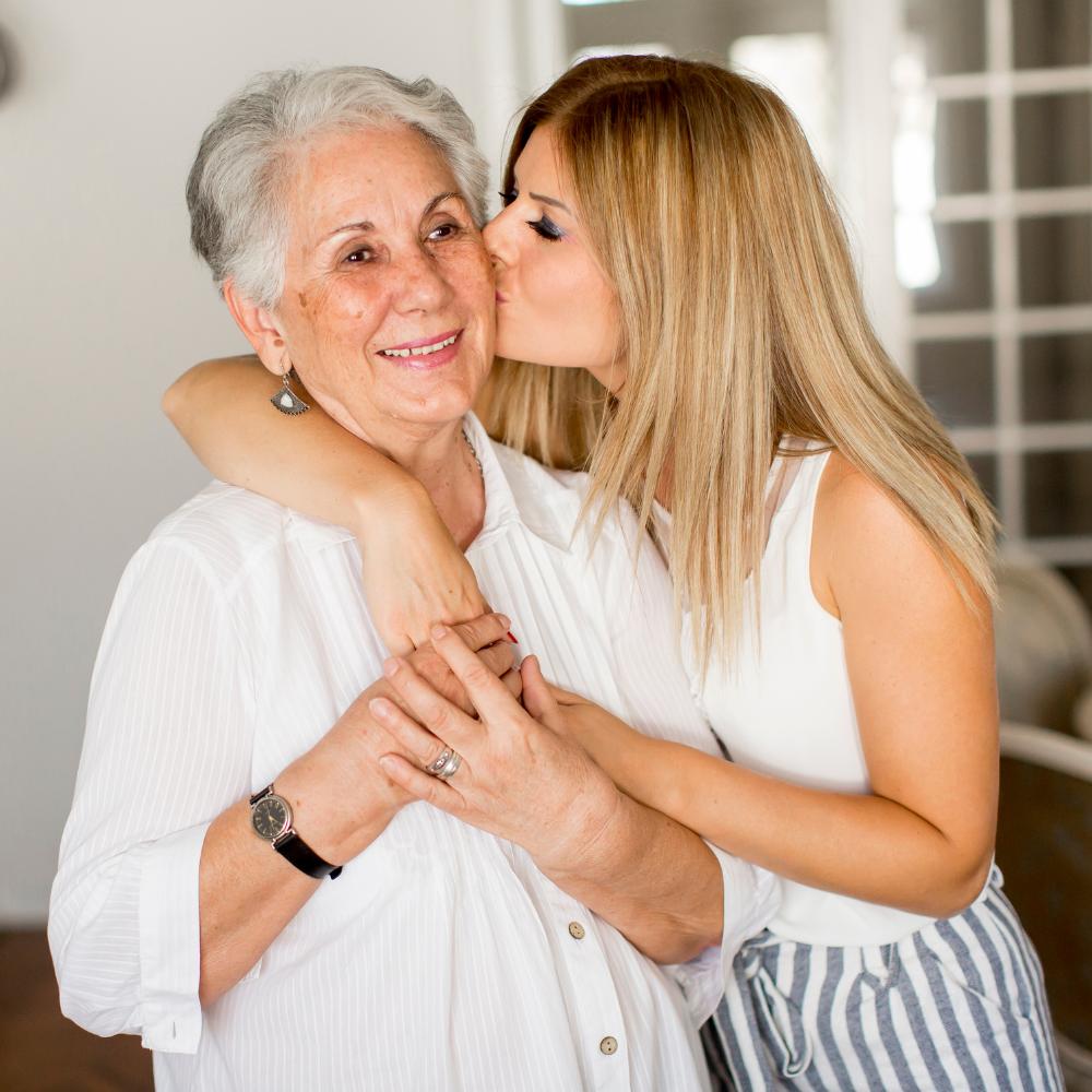 Smiling grandmother being hugged and kissed on the cheek by grown granddaughter.