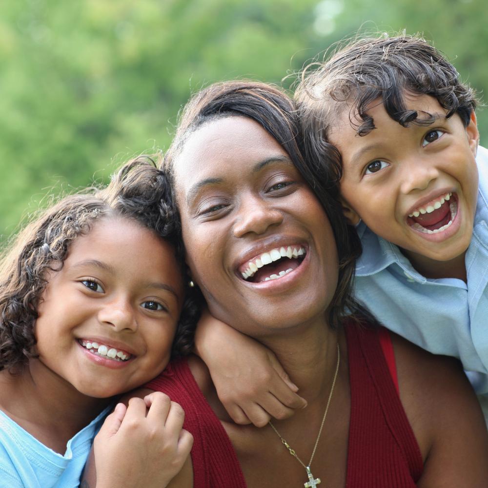 Mother being hugged by a son and daughter, all are smiling and look joyful